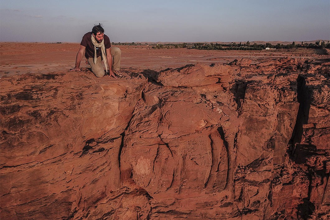 un chercheur sur l'un des promontoires rocheux : un dromadaire est grav&eacute; dans la paroi verticale. On distingue ses pattes et son tronc mais la t&ecirc;te a &eacute;t&eacute; abim&eacute;e par l'&eacute;rosion. 