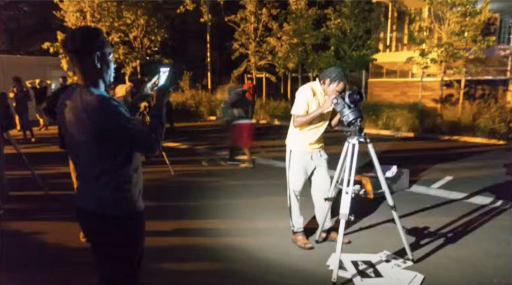 Un migrant observant dans un t&eacute;lescope sur un parking pendant qu'un autre le prend en photo